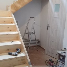 Tomasz M - Montaż drewnianych schodów wewnątrz budynku. Widoczne narzędzia: wkrętarka, drabina. Surowe drewno, jasne wnętrze. Etap budowy schodów.