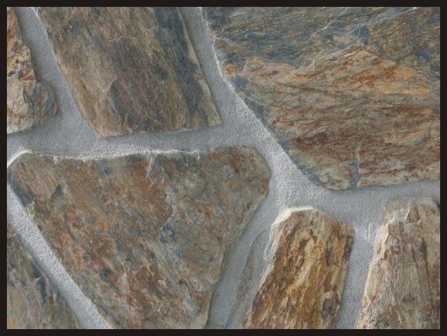 Fragment elewacji z nieregularnych, brązowo-szarych kamieni elewacyjnych połączonych jasnoszarą fugą.