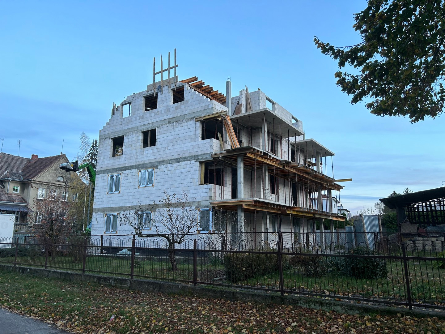 Wznoszony, trzypiętrowy budynek z białego bloczka, z widocznymi elementami konstrukcji stropów. Częściowo wstawione okna. Widok zza metalowego ogrodzenia.