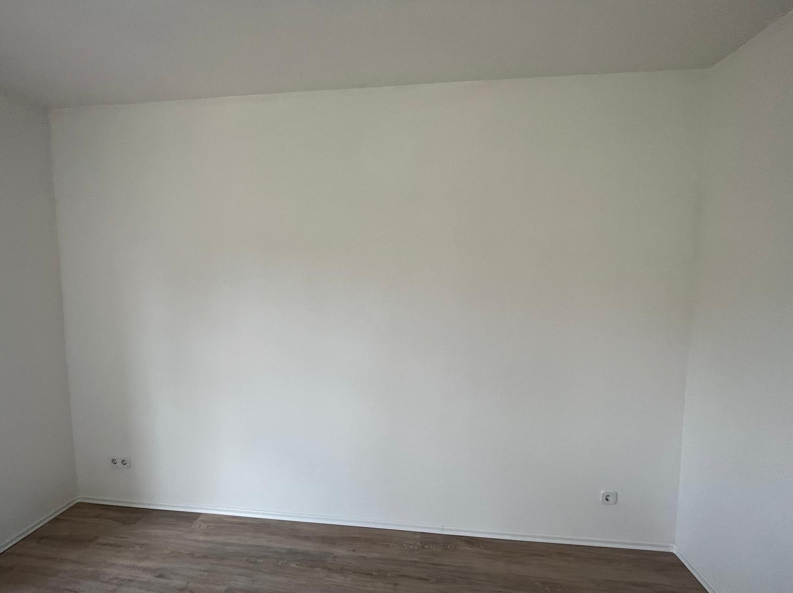 Pomalowane na biało wnętrze pokoju z panelami podłogowymi. Widoczne gniazdka elektryczne i listwa przypodłogowa. Świeżo po malowaniu.