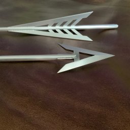 TADEUSZ ŚWIERZ TITANIUMSOUL - Dwie metalowe strzały z wyraźnymi spawami na brązowym tle. Strzały mają nowoczesny design, widoczne detale łączenia elementów.