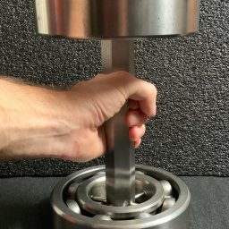 TADEUSZ ŚWIERZ TITANIUMSOUL - Metalowa konstrukcja spawana, przypominająca hantlę, trzymana w dłoni na tle szarej ściany. Widoczne spawy i elementy metalowe.