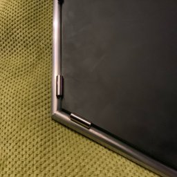 TADEUSZ ŚWIERZ TITANIUMSOUL - Fragment metalowej ramy z łącznikami, leżącej na zielonej, teksturowanej powierzchni. Widoczny spaw na rogu ramy. Precyzyjne wykonanie.