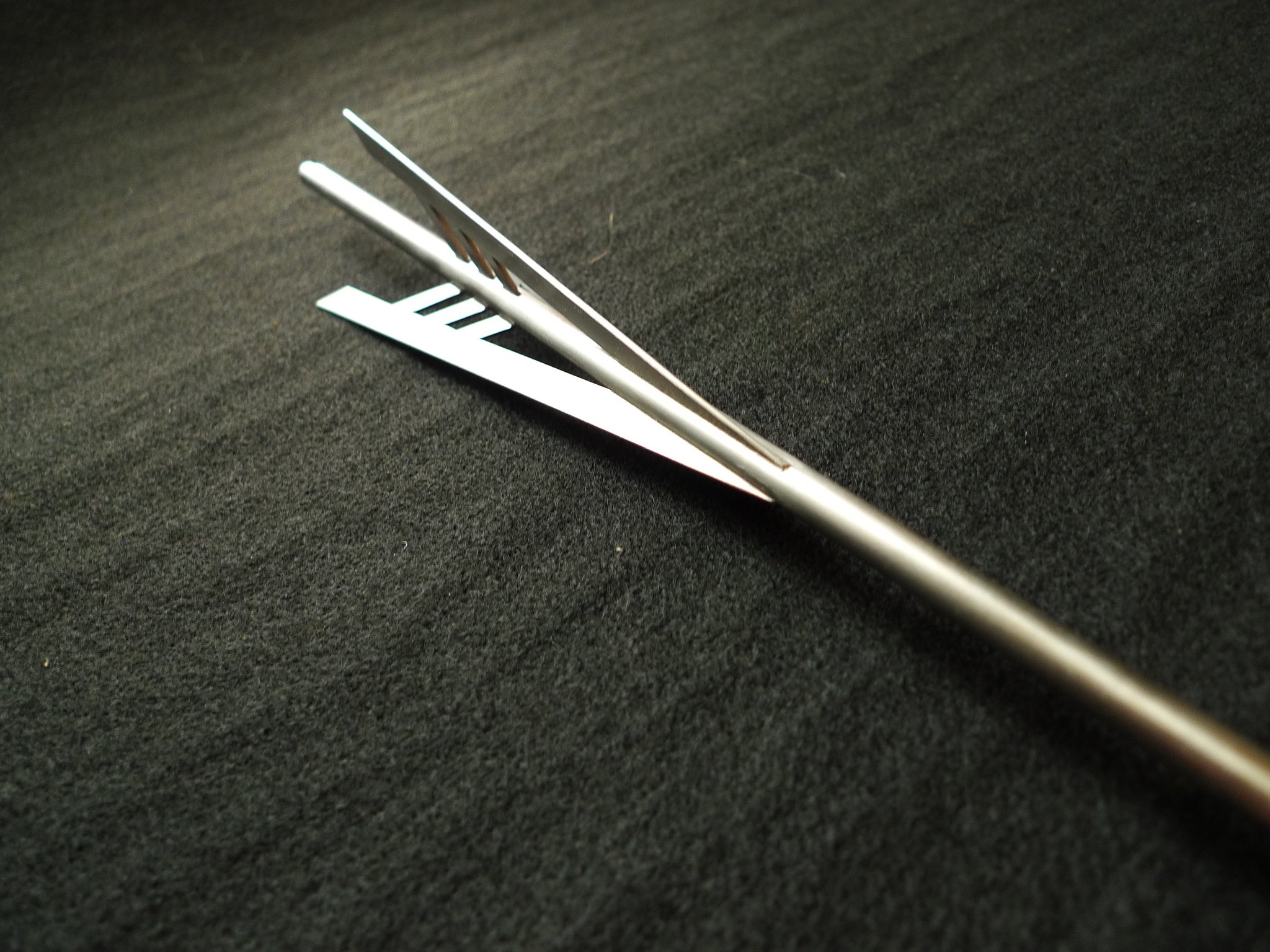 Precyzyjnie wykonany, srebrny uchwyt spawalniczy z trzema otworami, leżący na ciemnym, teksturowanym tle. Widoczne detale metalu i dokładność wykonania.