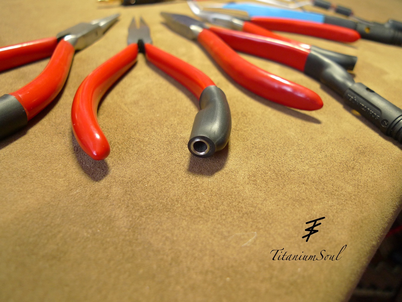 Szczypce z czerwonymi rękojeściami i czarnymi uchwytami, rozłożone na brązowym tle. Na pierwszym planie szczypce skierowane otworem w stronę widza.