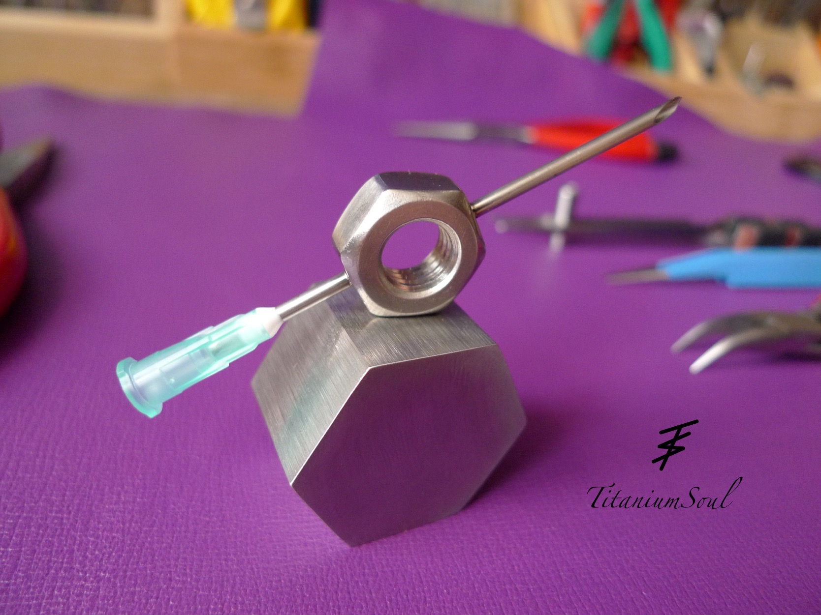 Nakrętka z igłą na metalowym sześcianie, fioletowe tło, narzędzia w tle. Precyzyjne łączenie metali, detale wykonania, obróbka metali.