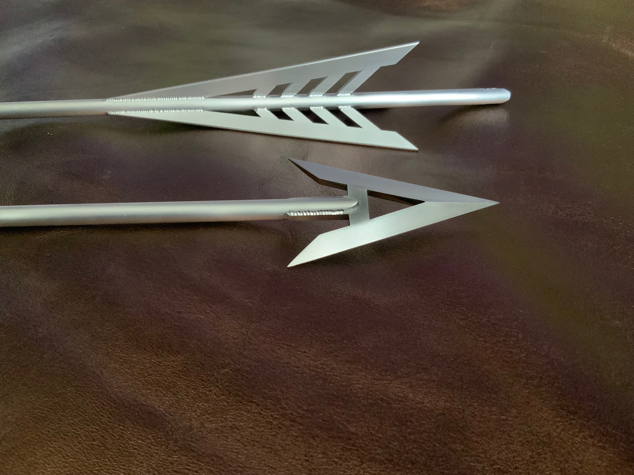 Dwie metalowe strzały z wyraźnymi spawami na brązowym tle. Strzały mają nowoczesny design, widoczne detale łączenia elementów.