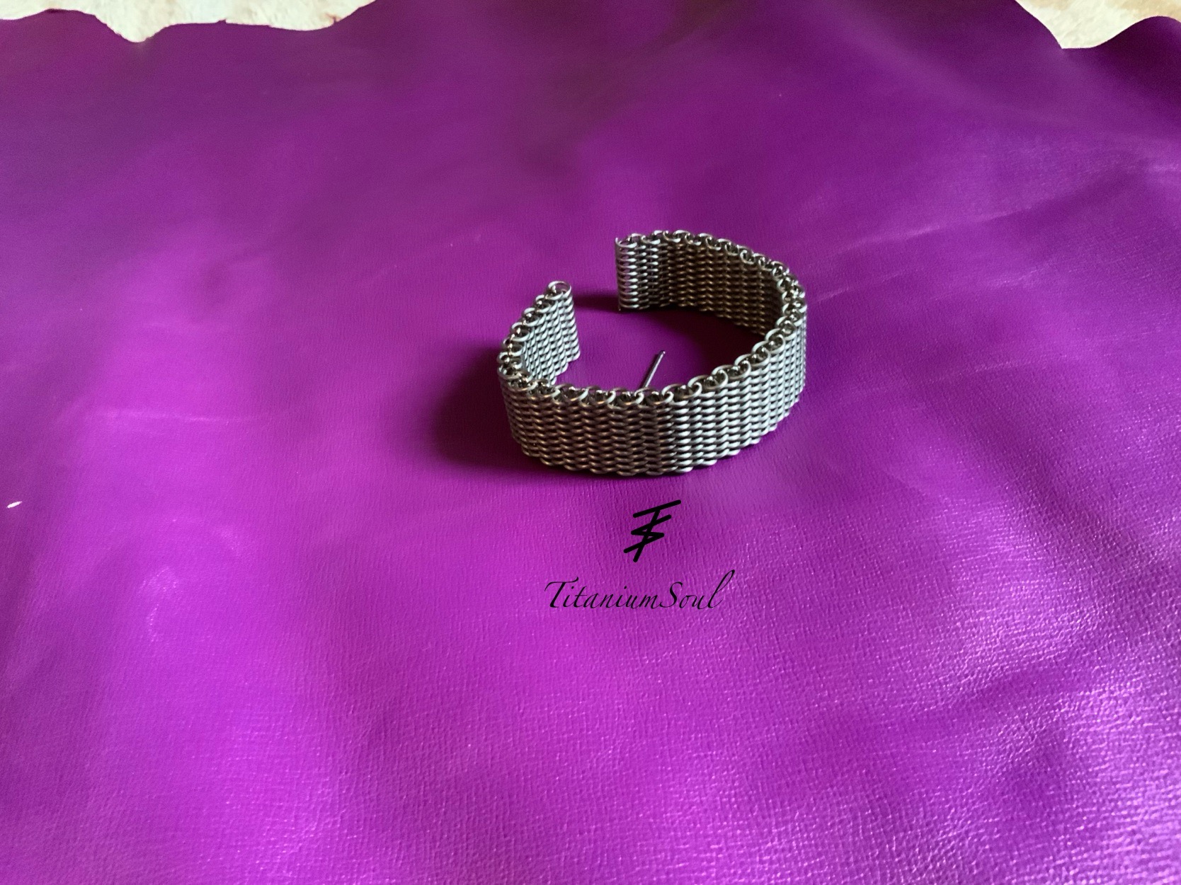Bransoleta z metalowej siatki na fioletowym tle, z widocznym logo 'Titanium Soul'. Precyzyjne wykonanie, gęsty splot. Unikalny design.
