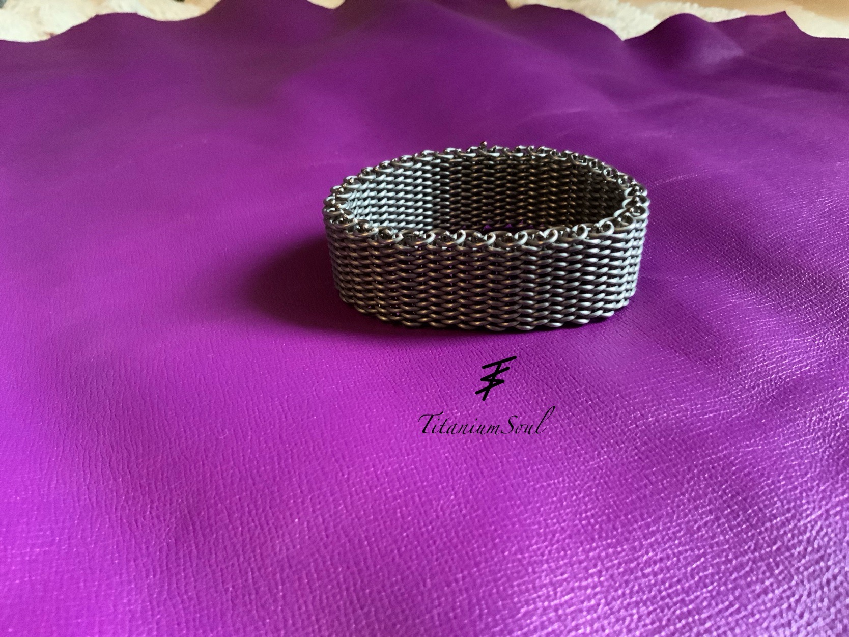 Metalowa bransoletka wykonana ze spawanych ogniw, leżąca na fioletowym tle. Widoczne logo 'Titanium Soul'.