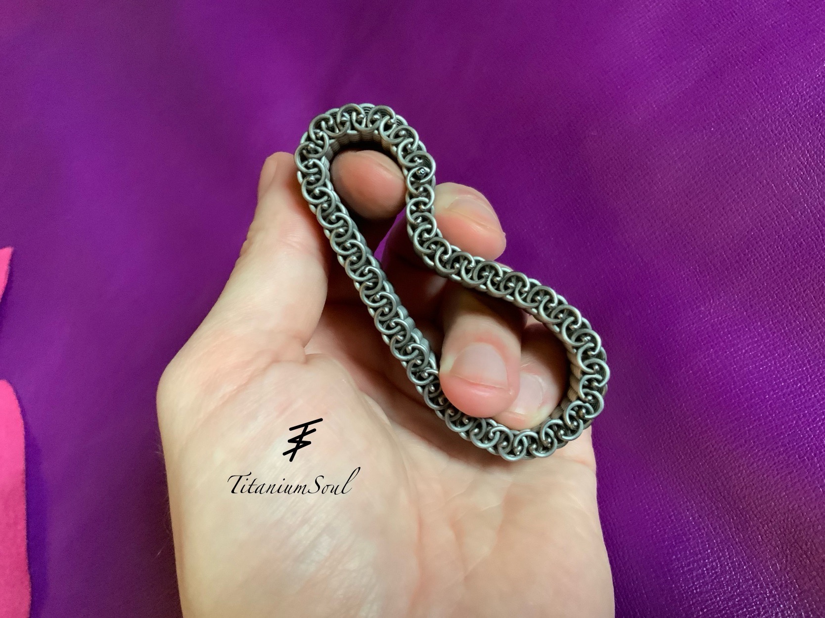 Ręcznie spawana, srebrna bransoletka ogniwkowa w kształcie pętli, trzymana w dłoni na fioletowym tle. Widoczne logo 'Titanium Soul'.