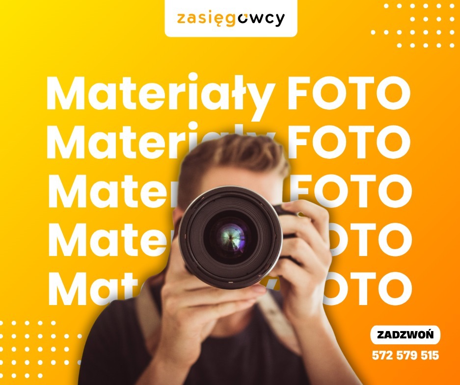Żółto-pomarańczowy baner reklamowy z fotografem celującym obiektywem w widza, hasłem 'Materiały FOTO' i numerem telefonu. Reklama firmy zasięgowcy.