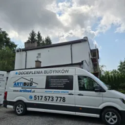 Biały budynek po renowacji elewacji, z zaparkowanym firmowym vanem Artibud z napisem 'Docieplenia Budynków' i numerem telefonu. Na dachu drabina.