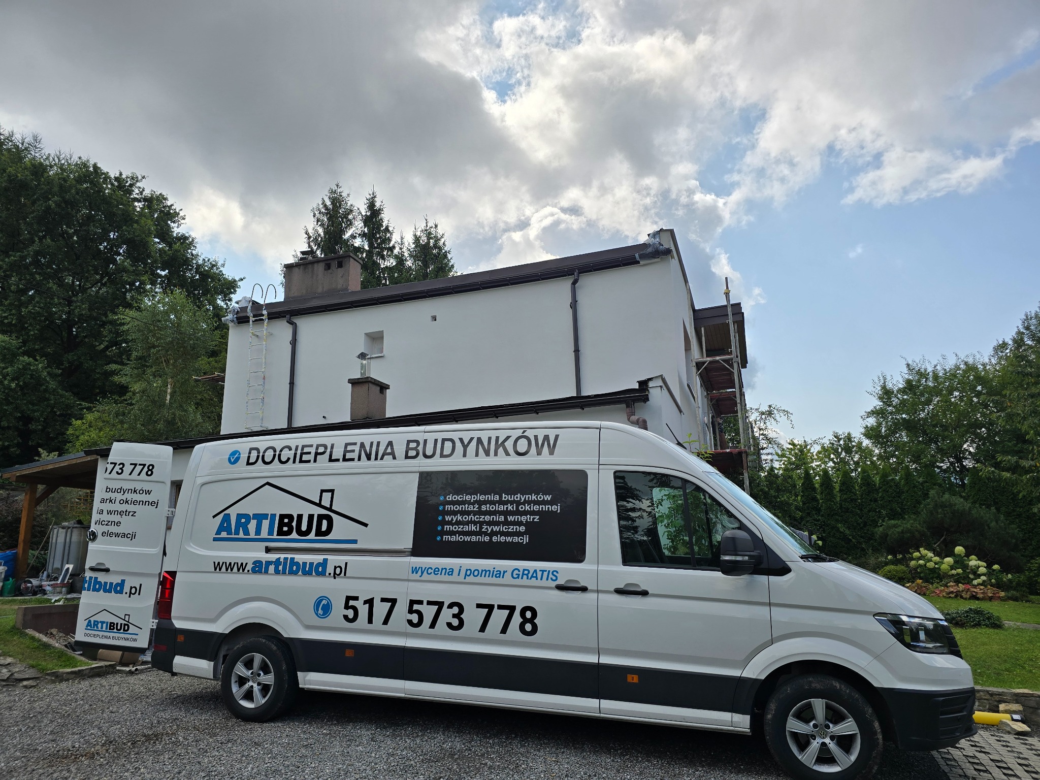 Biały budynek po renowacji elewacji, z zaparkowanym firmowym vanem Artibud z napisem 'Docieplenia Budynków' i numerem telefonu. Na dachu drabina.
