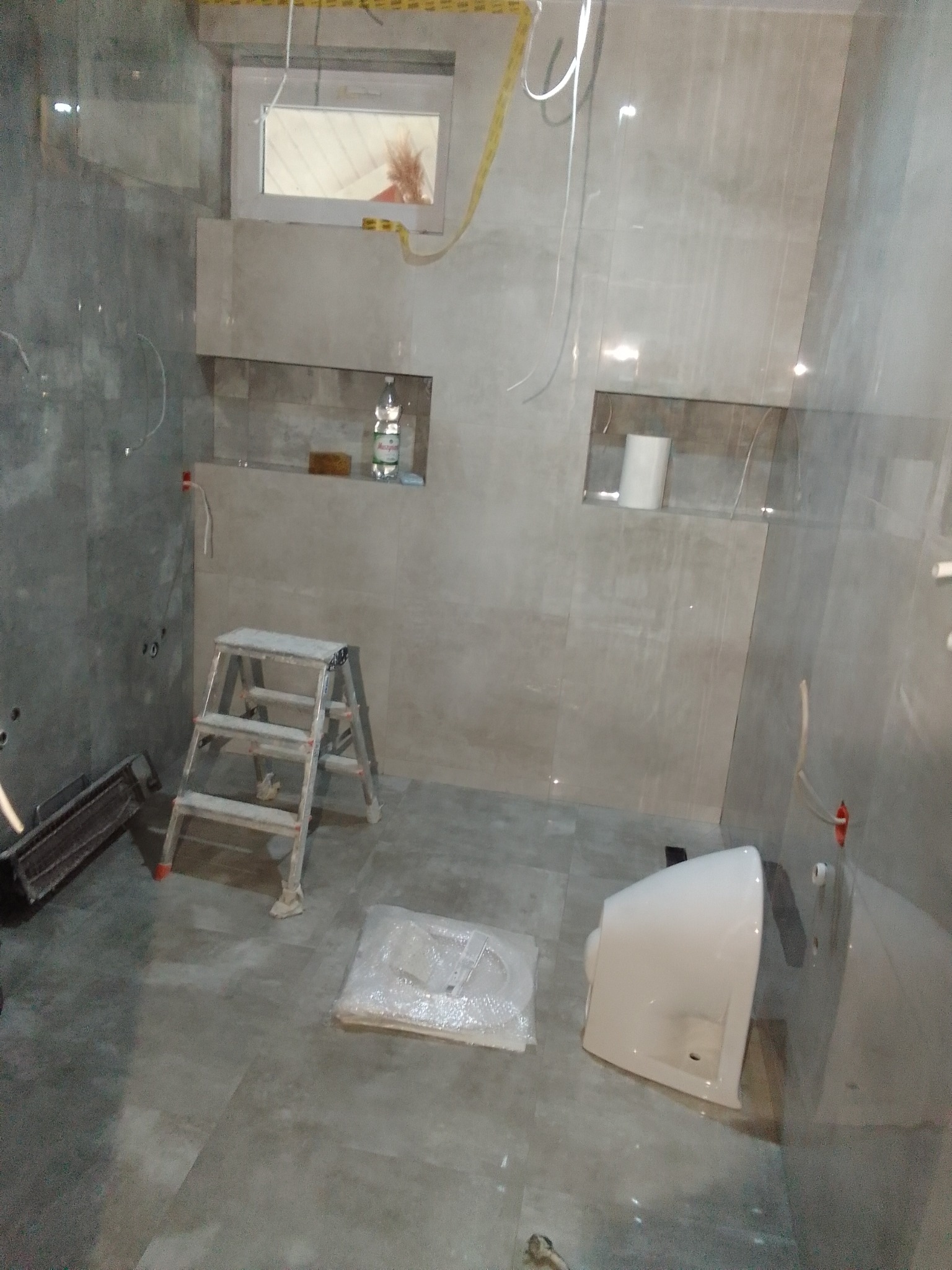 Wnętrze łazienki w trakcie prac glazurniczych w Harasiukach. Widoczne płytki na ścianach, drabina, umywalka i przygotowane wnęki.