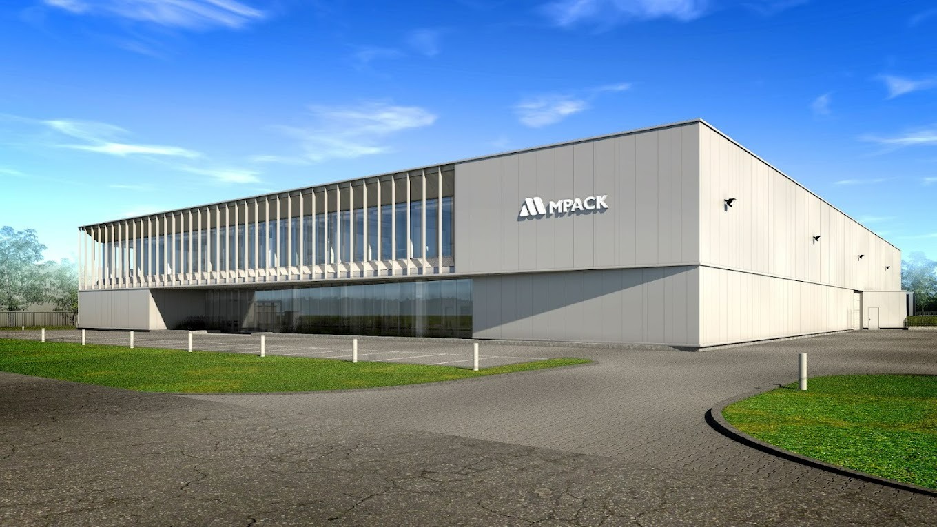 Nowoczesna hala przemysłowa z przeszkloną fasadą i logo 'MPACK' na elewacji, otoczona zielenią i asfaltową drogą dojazdową w słoneczny dzień.