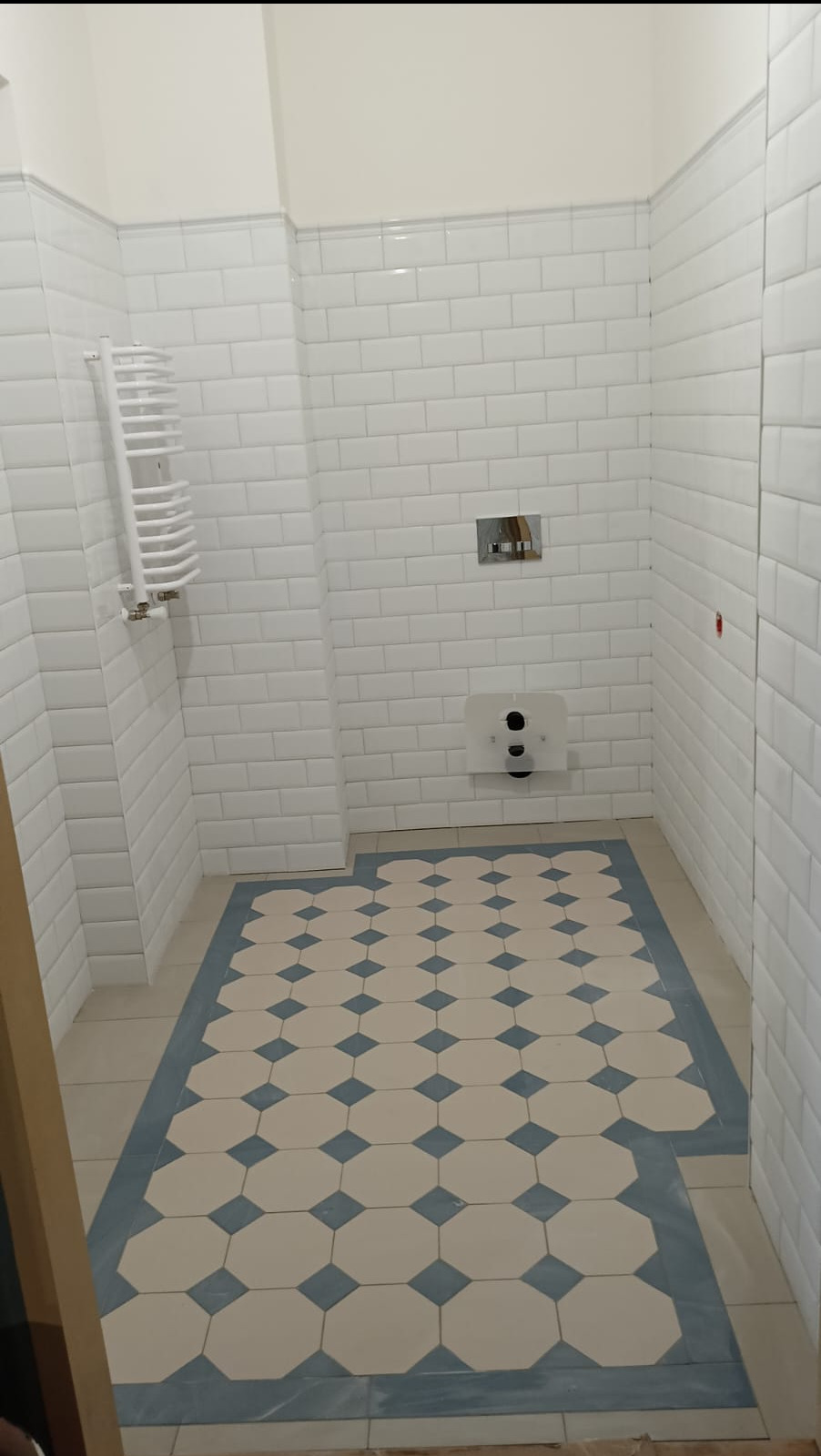 Biała łazienka w stylu retro z heksagonalną podłogą w beżowo-niebieską szachownicę. Na ścianach białe płytki imitujące cegiełki i grzejnik drabinkowy.