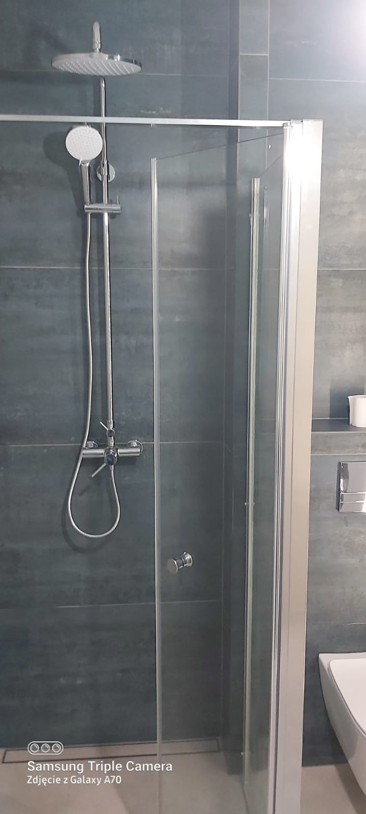 Nowoczesna kabina prysznicowa z deszczownicą i szarymi płytkami w łazience w Krotoszynie. Minimalistyczny design, chromowane elementy.