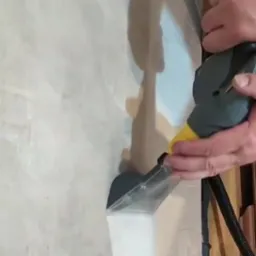 Czyszczenie tapicerki beżowego krzesła za pomocą parownicy z przezroczystą końcówką i żółtą dyszą. Widoczne dłonie operatora i fragment podłogi.