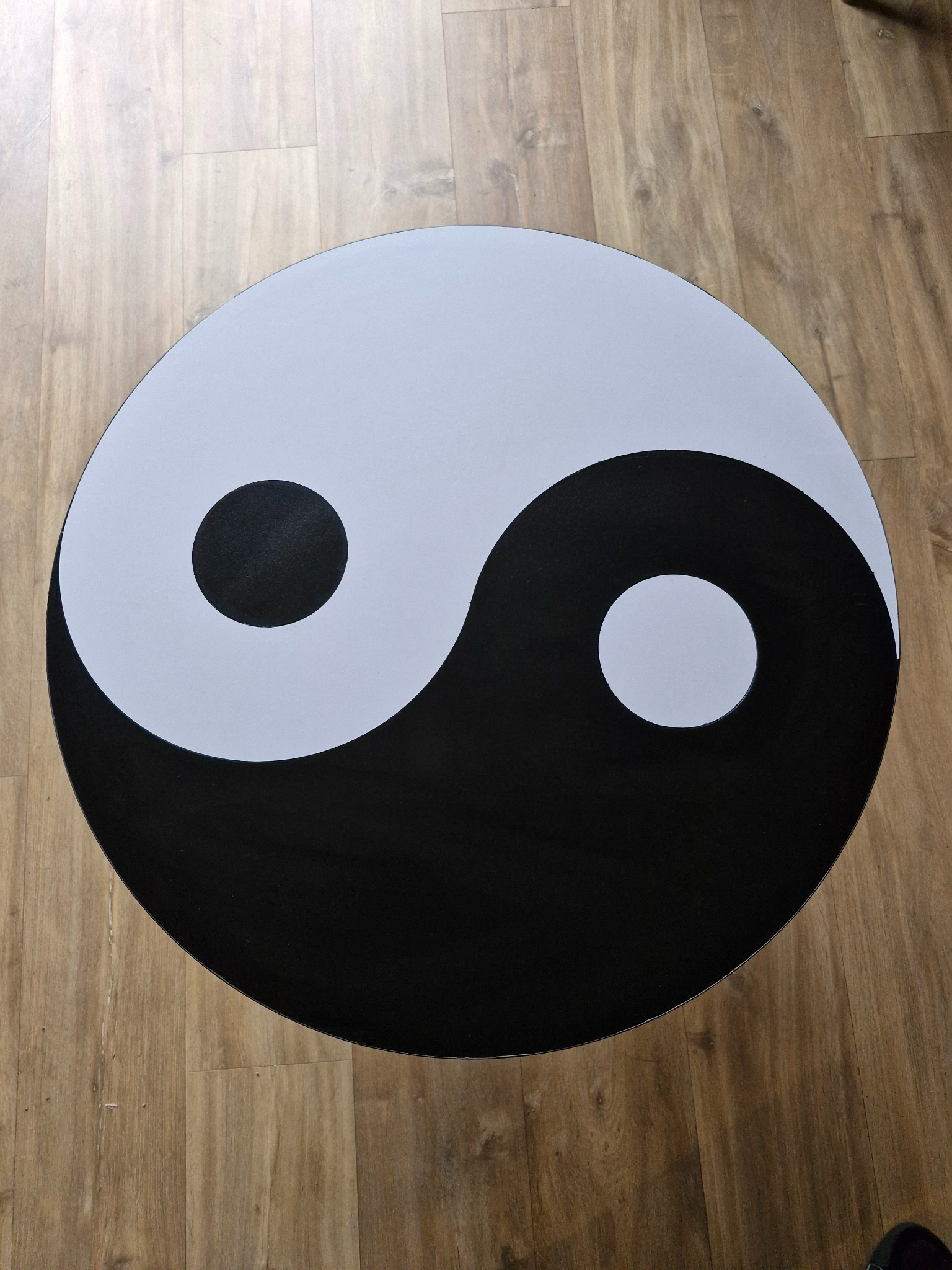 Okrągły stolik kawowy z motywem Yin Yang na drewnianej podłodze. Kontrastowe kolory i minimalistyczny design.