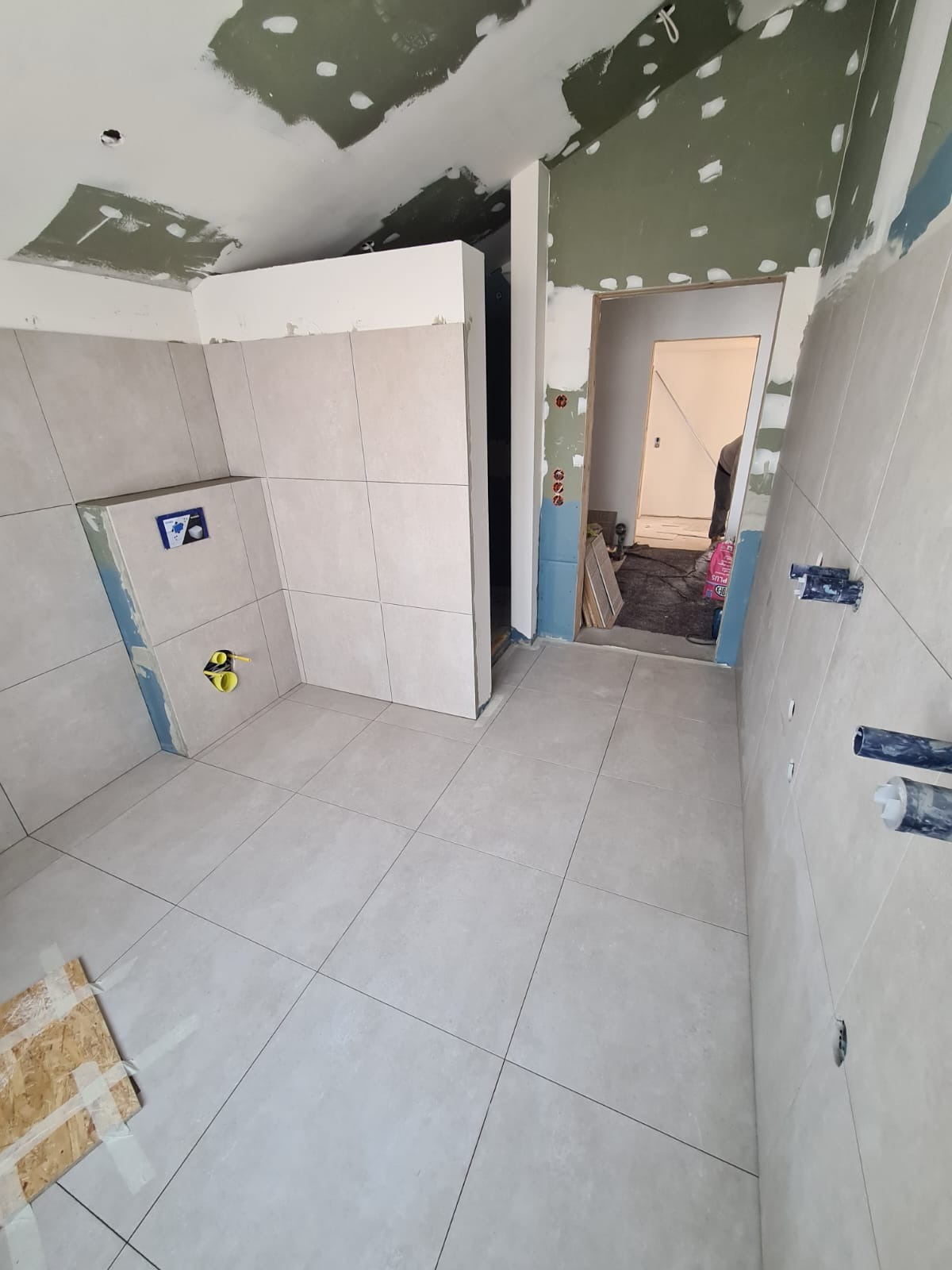 Remont łazienki w trakcie: ułożone jasne płytki podłogowe i ścienne, widoczne instalacje podtynkowe, przygotowane ściany do malowania, surowy stan wykończenia.