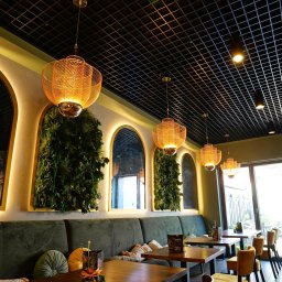 BUDART EXPERT ARTEM SKLIAR - Stylowe wnętrze restauracji z zieloną ścianą, lustrami w złotych ramach i dekoracyjnymi lampami. Widoczny ciemny sufit z kratką i drewniane stoły.