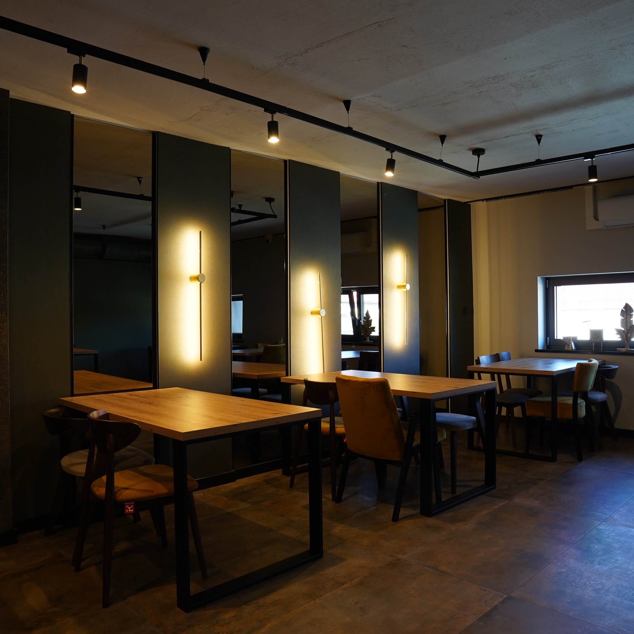 Nowoczesne wnętrze biurowe z drewnianymi stołami, krzesłami i oświetleniem LED. Lustra na ścianach optycznie powiększają przestrzeń. Minimalistyczny design.