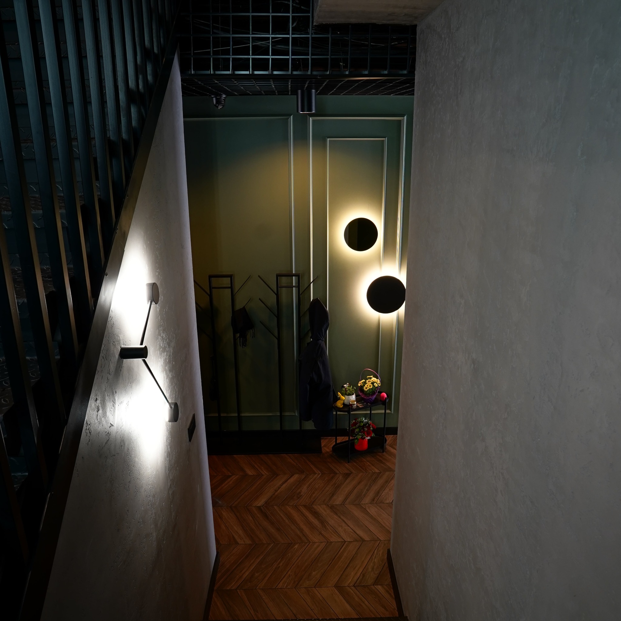 Nowoczesny przedpokój z parkietem w jodełkę, oświetleniem punktowym i ścianami w odcieniach szarości i zieleni. Widok z góry na eleganckie wykończenie wnętrza.