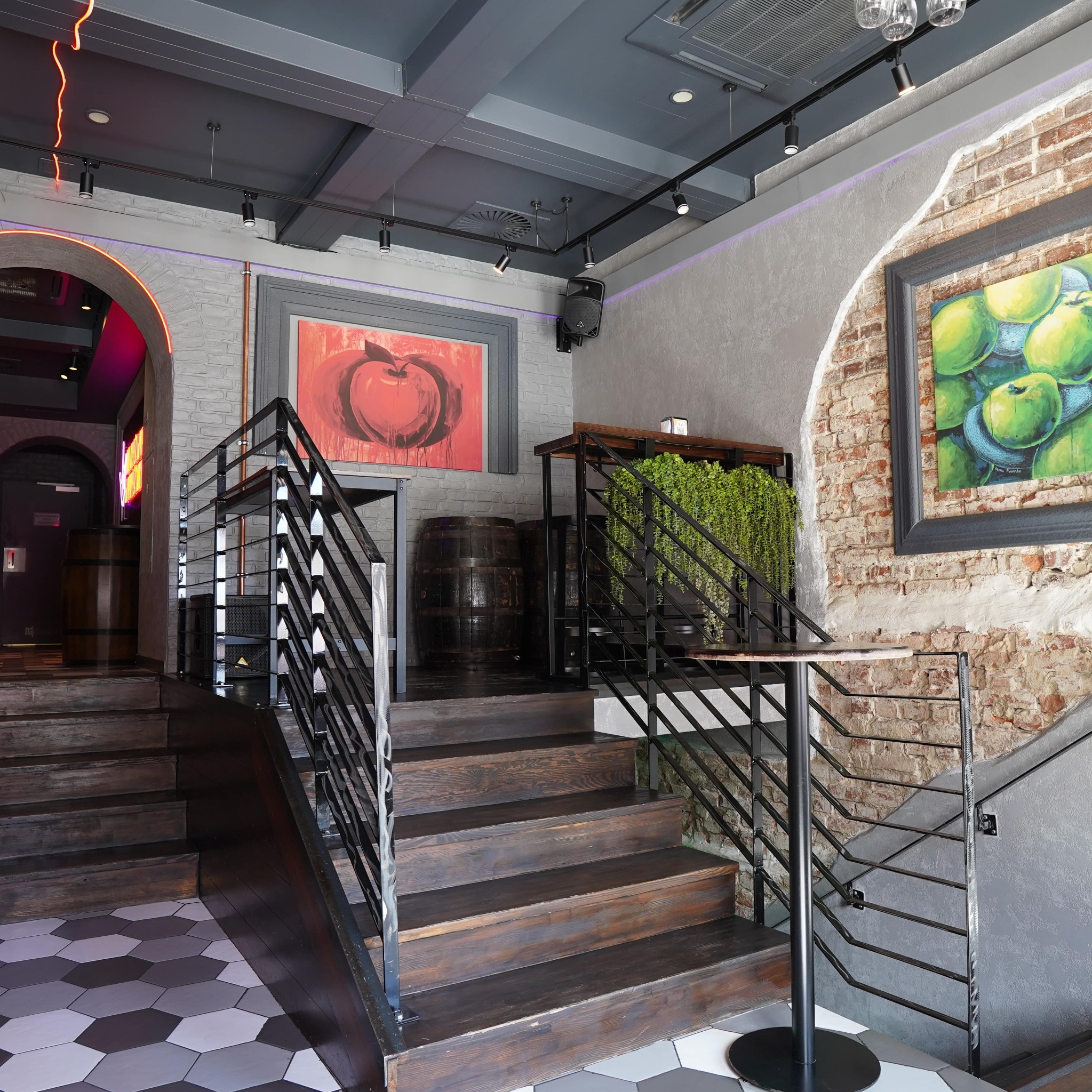 Schody z ciemnego drewna z metalową balustradą w loftowym wnętrzu. Na ścianach cegła i beton, obrazy w ramach. Podłoga w heksagonalne płytki.