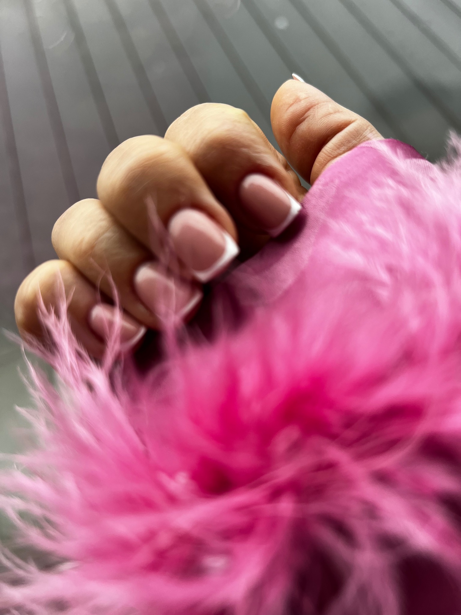 Dłoń z perfekcyjnym manicure francuskim na tle różowego boa z piór. Delikatne, jasne paznokcie z białymi końcówkami. Estetyczny i zadbany wygląd.