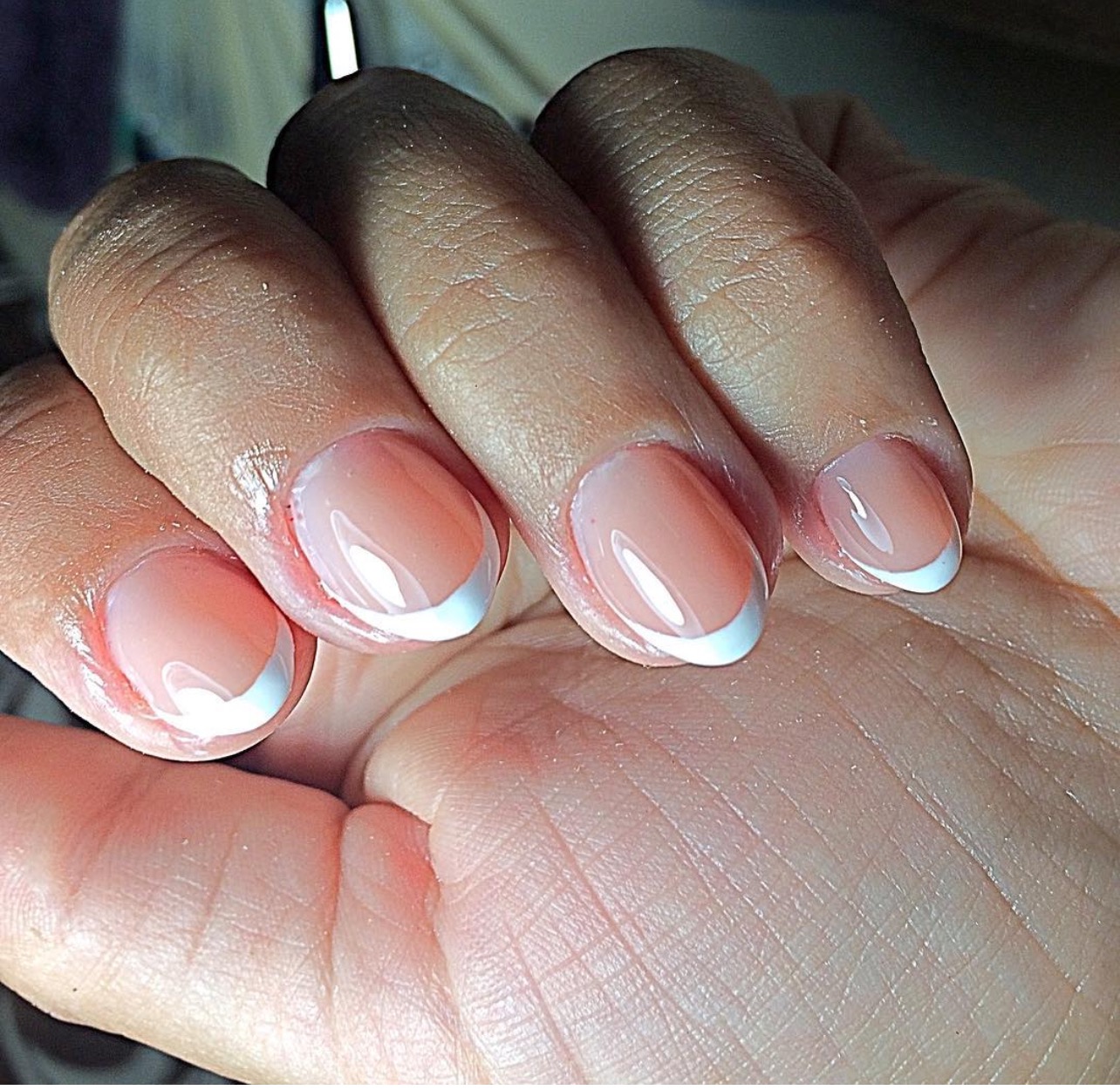 Dłoń z perfekcyjnym manicure francuskim. Delikatny róż i śnieżnobiała końcówka tworzą elegancki, zadbany wygląd. Widoczne detale skóry dłoni.