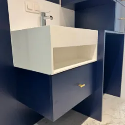 Nowoczesna, granatowo-biała umywalka z szafką i złotymi uchwytami, na tle marmurowej podłogi. Minimalistyczny design z widocznymi detalami armatury i oświetlenia.