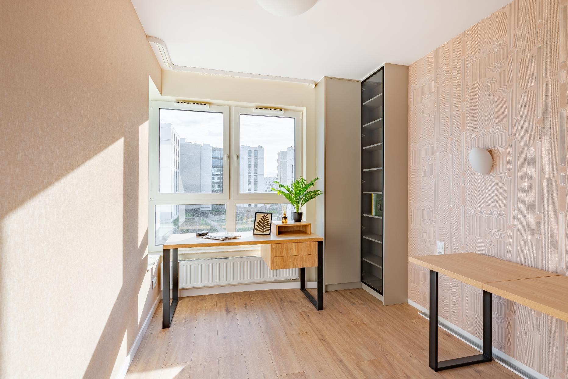 Jasny pokój z biurkiem z drewna i czarnymi nogami, regał z przeszklonymi drzwiami i tapeta w geometryczny wzór. Nowoczesne wnętrze z rośliną doniczkową na biurku.