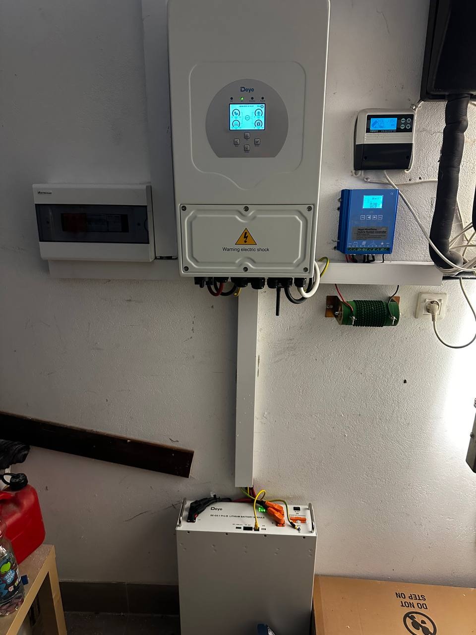 Kompletna instalacja fotowoltaiczna w garażu: biały inwerter Deye z ekranem, akumulator litowo-jonowy i zabezpieczenia na ścianie. Widoczne okablowanie i elementy montażowe.