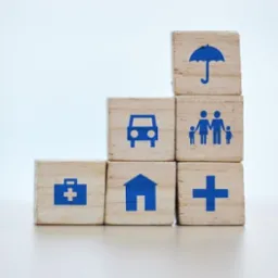 Drewniane kostki z ikonami: parasol, auto, rodzina, dom, apteczka, krzyż. Symbolika ubezpieczeń na życie, mieszkania, OC i zdrowotnych. Jasne tło.