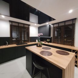 K2-ROL KAROL KRUSZCZAK - Nowoczesna kuchnia z drewnianymi żaluzjami w oknach. Czarne szafki i jasny blat tworzą kontrast. Widoczne detale wystroju i oświetlenie.