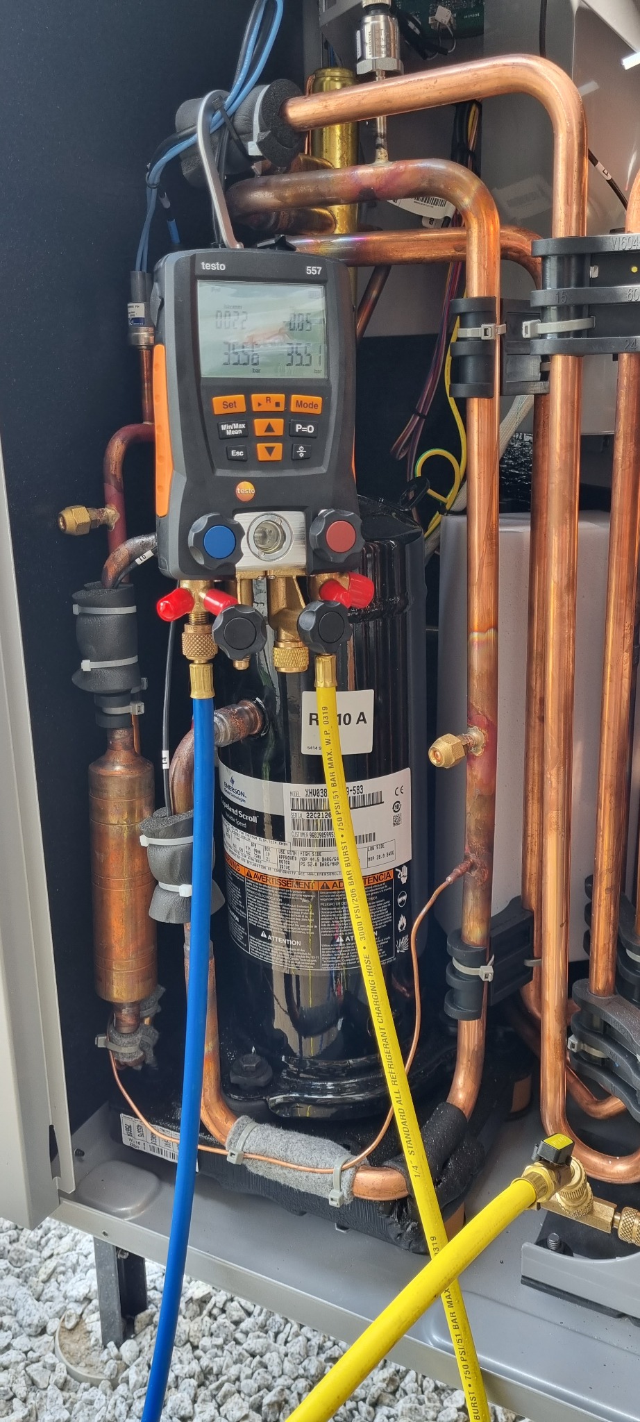 Pomiar parametrów pracy pompy ciepła za pomocą elektronicznego kolektora Testo 557. Widoczne miedziane rury, przewody pomiarowe i sprężarka. Diagnostyka w trakcie serwisu.