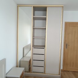 WEST ART Pracownia Meblarska - Jasna szafa przesuwna z lustrem i złotymi obramowaniami, wkomponowana w aranżację sypialni z widocznym łóżkiem i szafką nocną.