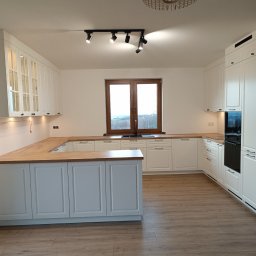 WEST ART Pracownia Meblarska - Jasna kuchnia w stylu klasycznym z drewnianym blatem. Białe szafki z ciemnymi uchwytami. Na podłodze panele imitujące drewno. Okno z widokiem na zewnątrz.