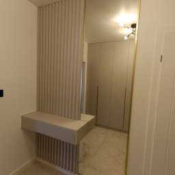 WEST ART Pracownia Meblarska - Nowoczesna zabudowa przedpokoju z lustrem w złotej ramie i konsolą z lamelami w odcieniach beżu. Widoczne szafy w tle i marmurowa posadzka.
