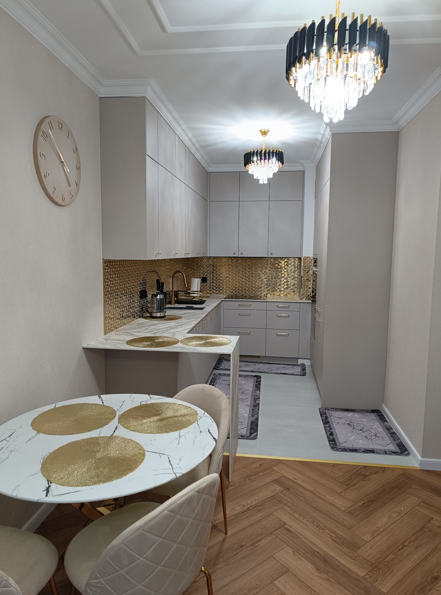 Elegancka, beżowa kuchnia na wymiar z złotymi akcentami: mozaika nad blatem, armatura i detale. Okrągły stół z marmurowym blatem i beżowymi krzesłami. Parkiet w jodełkę.