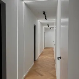 Nowoczesny korytarz z oświetleniem LED wzdłuż ścian i sufitu, parkiet w jodełkę. Realizacja wykończenia wnętrz w Poznaniu.