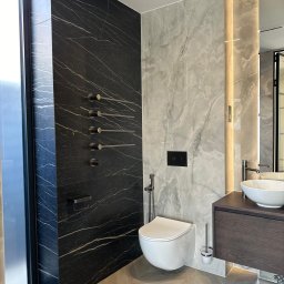 Ruzop - Nowoczesna łazienka z marmurowymi płytami, czarną ścianą z grzejnikiem drabinkowym i drewnianą szafką pod umywalką. Parkiet ułożony w jodełkę.