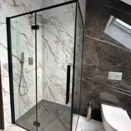 Nowoczesna kabina prysznicowa z czarnymi profilami i deszczownicą, marmurowe płytki w odcieniach bieli i szarości, wisząca toaleta w wykończonej łazience na poddaszu.