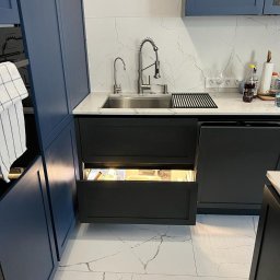 Ruzop - Nowoczesna kuchnia z granatowymi szafkami i marmurowym blatem. Otwarta szuflada pod zlewem z oświetleniem LED. Bateria kuchenna ze stali nierdzewnej.