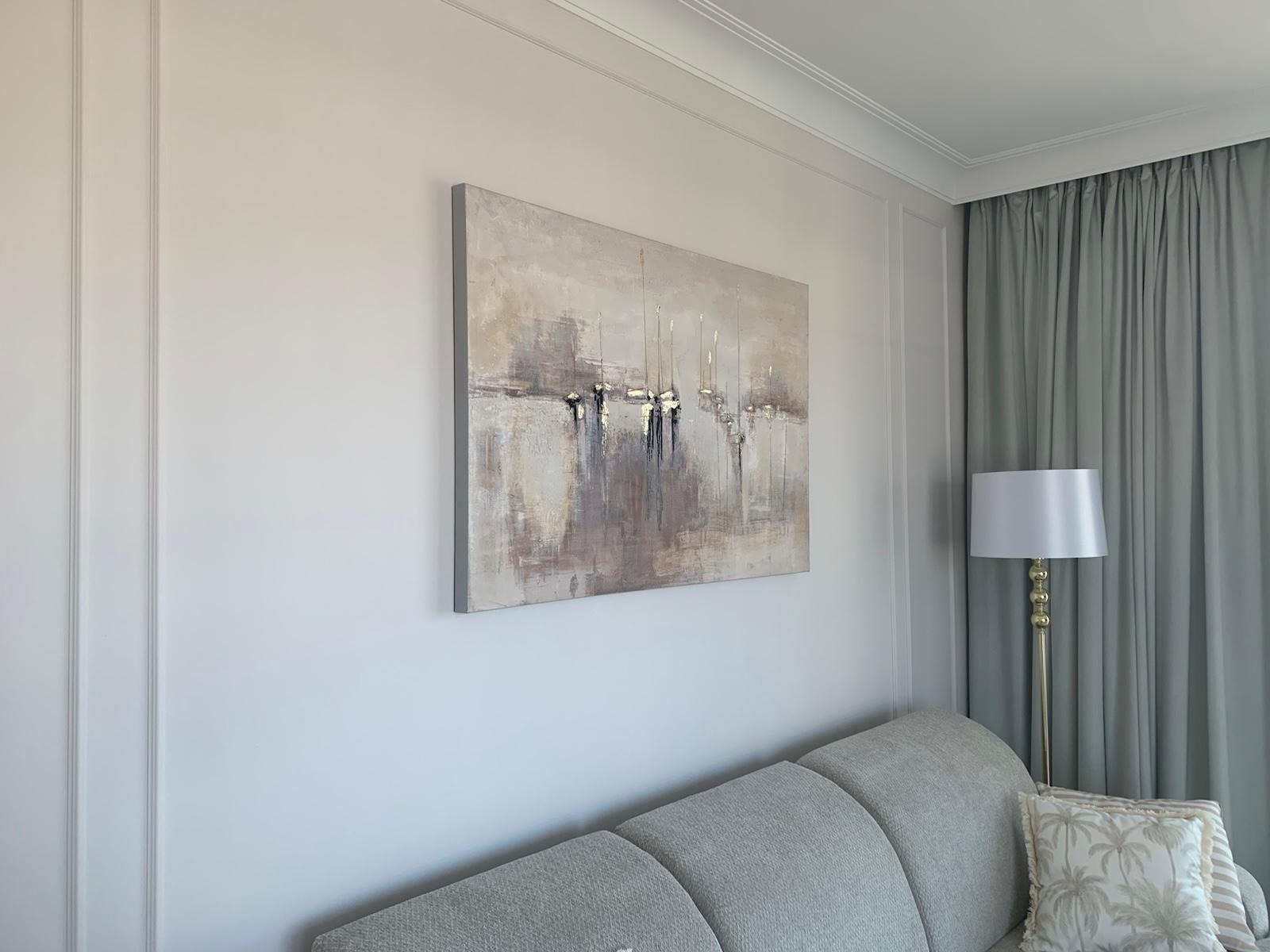 Abstrakcyjny obraz z motywem żaglówek w stonowanych barwach, zawieszony na ścianie w salonie z szarą sofą i lampą podłogową.