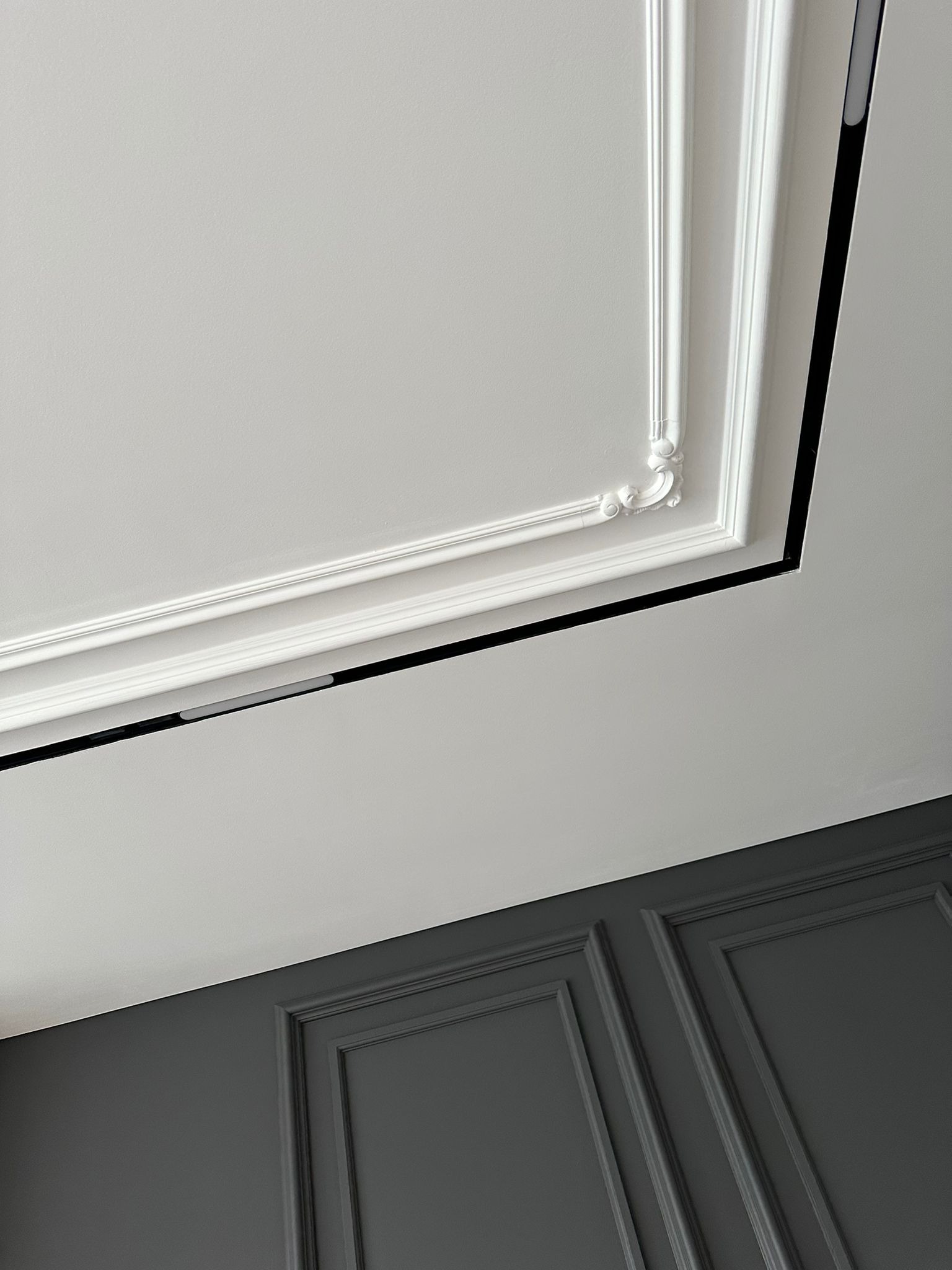 Szare panele ścienne i biały sufit z dekoracyjną sztukaterią. Ujęcie pod kątem, podkreślające połączenie klasyki i nowoczesności.