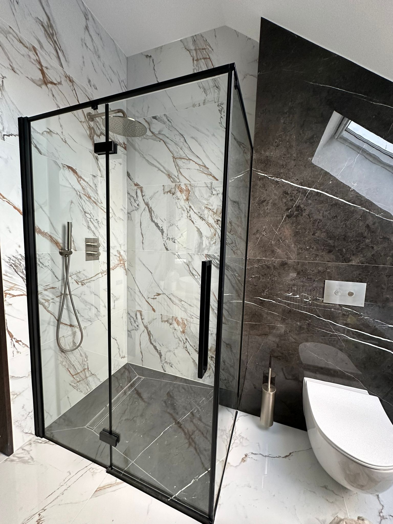 Nowoczesna kabina prysznicowa z czarnymi profilami i deszczownicą, marmurowe płytki w odcieniach bieli i szarości, wisząca toaleta w wykończonej łazience na poddaszu.