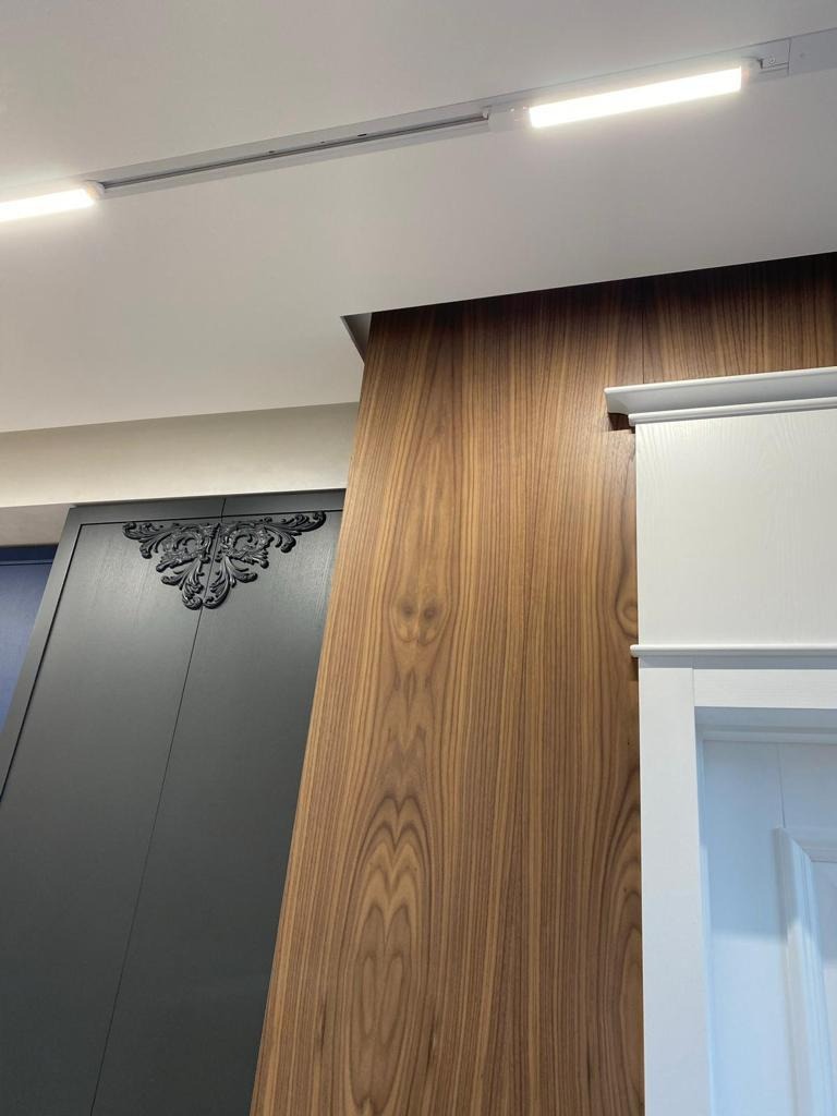 Wykończenie wnętrza w Poznaniu: Detal zabudowy meblowej z forniru orzechowego, czarny, zdobiony front szafy i białe drzwi z profilowanymi listwami.