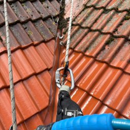 CLEAN HOUSE Radosław Myśliwiec - Czerwona dachówka częściowo pokryta mchem, lina z karabińczykiem, fragment rynny. Górny kadr ukazuje obszar po czyszczeniu, dolny przed.