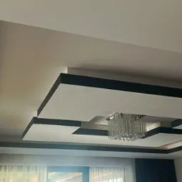 Nowoczesny sufit podwieszany z oświetleniem punktowym i listwami dekoracyjnymi w kolorze grafitowym, tworzący geometryczny wzór. Wykończenie wnętrza.